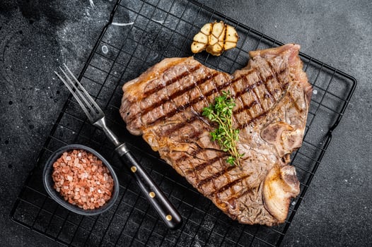 Grilled T-bone or Porterhouse beef meat Steak on a rack. Black background. Top view photo