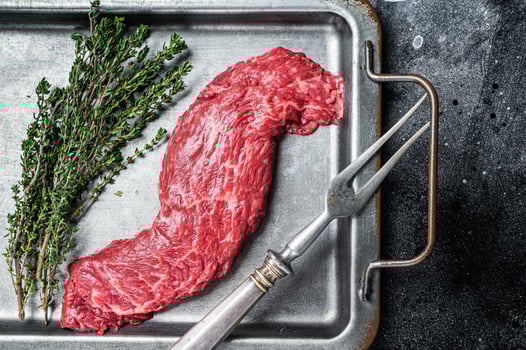 Raw fresh meat Steak Machete, skirt with thyme on steel tray. Black background. Top view photo