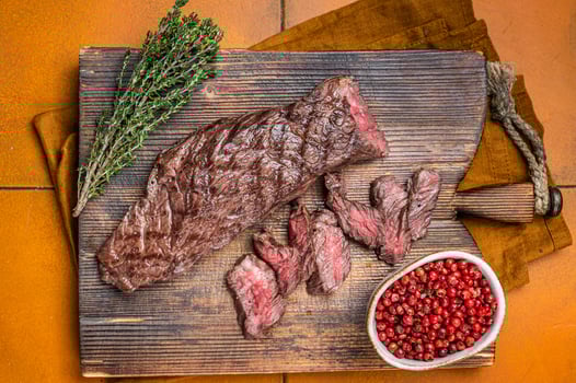 Grilled Medium Rare Machete or skirt beef meat steak on wooden cutting board. Orange background. Top view photo