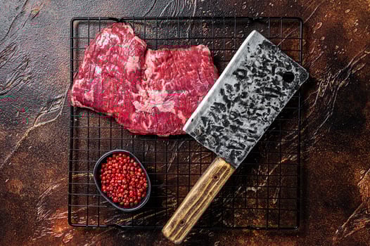 Raw skirt beef steak on meat cleaver. Black background. Top view photo
