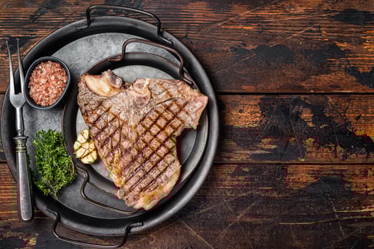 BBQ Grilled T-bone or Porterhouse beef meat Steak on a steel tray with herbs. Wooden background. Top view. Copy space photo