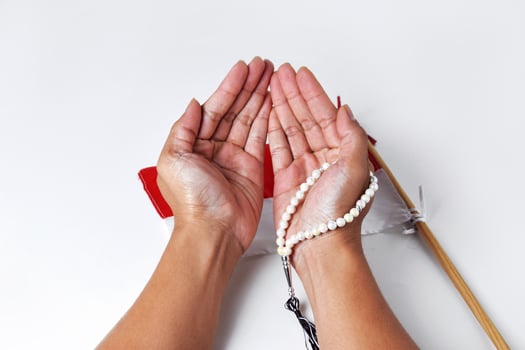 People's hands are praying using prayer beads with the red and white flag photo