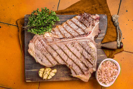 BBQ Roast T bone or Porterhouse beef meat Steak on a wooden board with spices. Orange background. Top view photo
