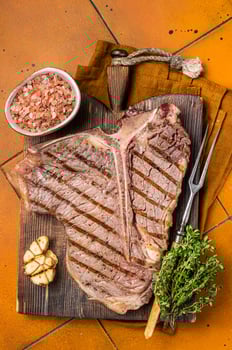 BBQ Roast T bone or Porterhouse beef meat Steak on a wooden board with spices. Orange background. Top view photo