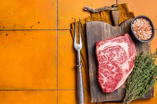 Prime Raw wagyu Rib Eye beef meat steak on wooden board. Orange background. Top view. Copy space photo
