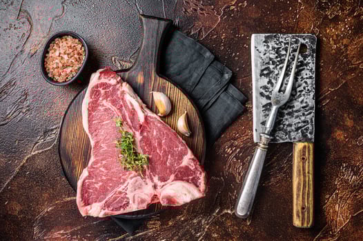 Raw Porterhouse steak, marbled beef meat on a wooden board. Dark background. Top view photo
