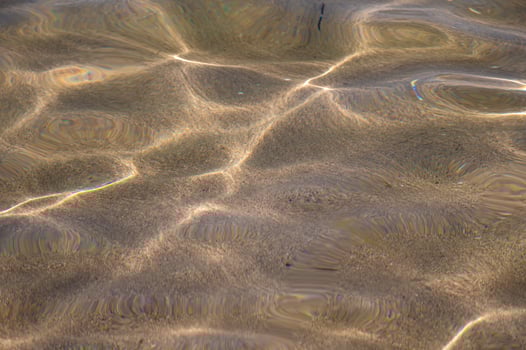Through the transparent water of the ocean or sea you can see the sandy bottom with ridges of sand. Sun glare and ripples. View from above photo