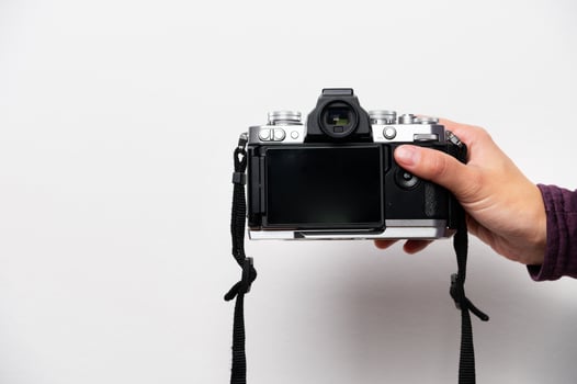 Hand holding retro camera with neck strap on white background. Vintage things, mixing old and modern style in camera design photo