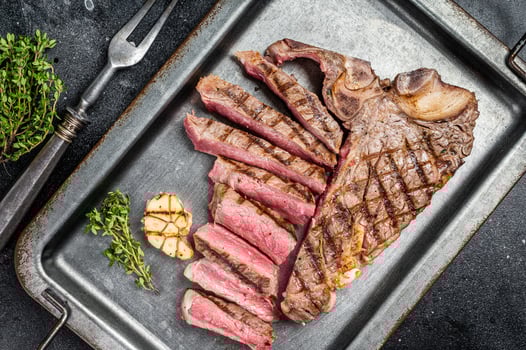 Medium rare Grilled T-Bone Steak, Florentine steak sliced in a steel tray. Black background. Top view photo