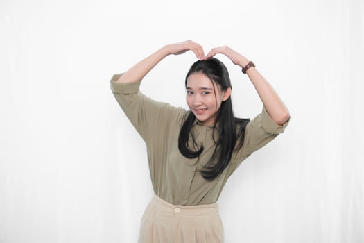 The smiling expression of an Indonesian Asian woman in green makes a love symbol photo