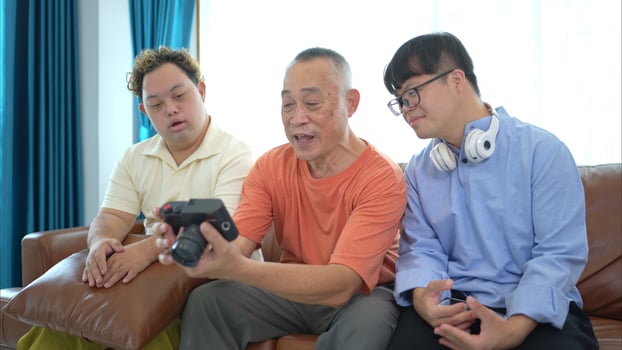 On their day off, the grandfather and grandson look at old photos on camera in living room of house