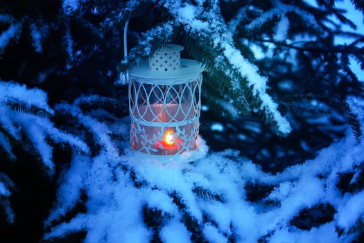 Decorative Christmas lantern with burning candle hanging on snow-covered fir- tree branch in a winter park. New year festive card, poster, postcard design. photo