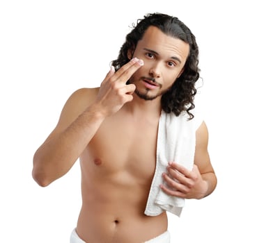 A young man applies skincare product on his face in a minimalist setting photo