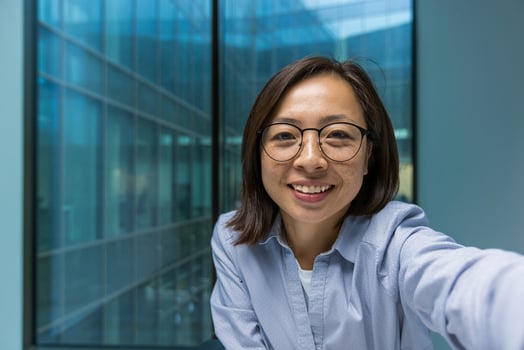 Asian businesswoman in office taking selfie with phone, showcasing confidence and approachability. Smiling expression represents modern professionalism and effective communication. photo