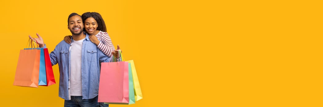 Cheerful Young Black Couple Posing With Shopping Bags In Hands Over Yellow Background, Happy Millennial African American Man And Woman Carrying Purchases, Enjoying Seasonal Sales, Copy Space photo