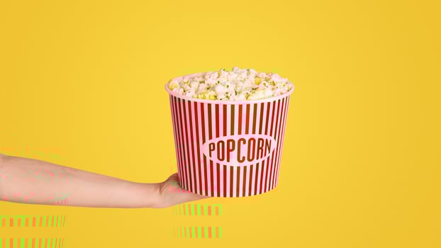 Millennial girl holding bucket of fresh crunchy popcorn over pink background, closeup photo