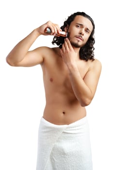 A young man with curly hair grooming his beard using an electric trimmer photo