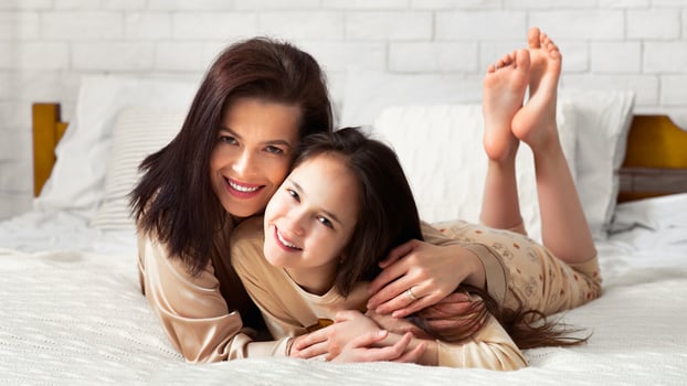Parent child love. Happy young woman embracing her teenage daughter on bed, panorama photo