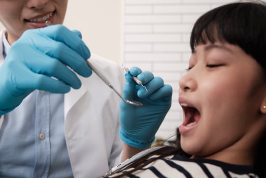 A young Asian male pediatric dentist checks and examines a little Thai girl's teeth in dental clinic, well-being mouth oral hygiene, and professional orthodontic healthcare work in a kid hospital. photo