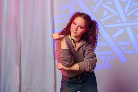 A young woman with curly red hair poses in front of a geometric projection photo
