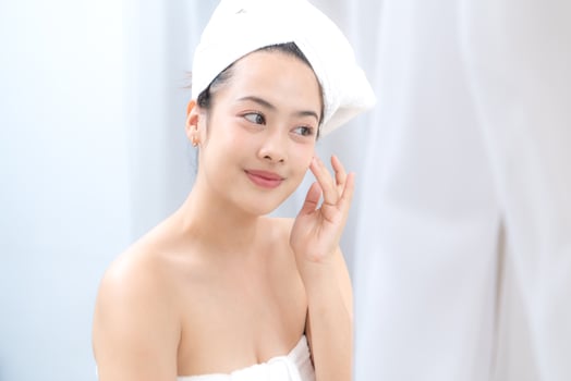 Asian young woman with towel wrapped on head and body applying makeup after shower, Morning beauty routine before work photo