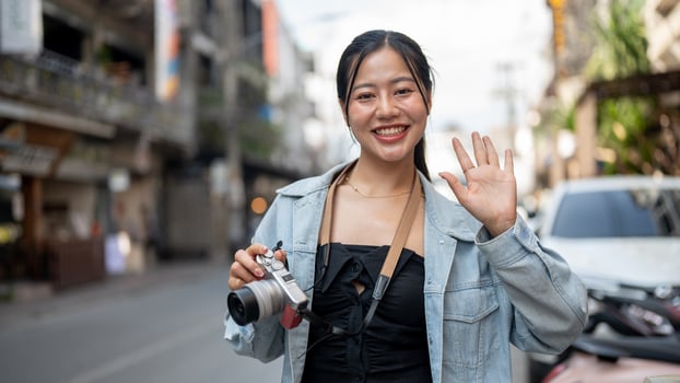 A happy Asian female tourist enjoying taking photos while exploring the city, smiling at the camera.