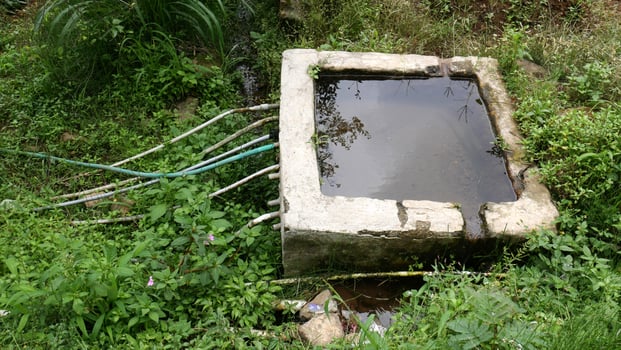 Irrigation system in the countryside with concrete water tank as a water storage, with some plastic pipes used for distribution to farms or households. Wild plants grow abundantly around it. photo