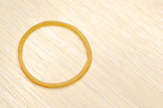 A detailed closeup view of a bright Yellow Rubber Band positioned on a Wooden Surface photo