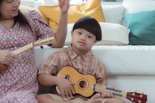 A special child with his mom plays the ukulele in the living room of the house photo