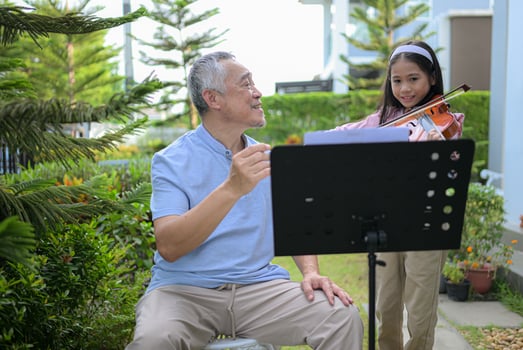 A girl violinist and her grandfather practice music together in the garden at home photo