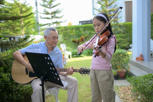 A girl violinist and her grandfather practice music together in the garden at home photo