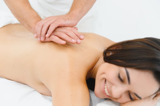 Woman enjoying professional body massage at a modern spa salon. Relaxed young lady lying on a massage table while a skilled masseur is gently massaging her back. Beauty, health, pleasure, concept photo