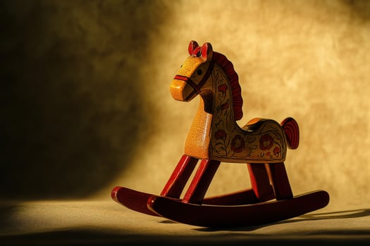A beautifully crafted wooden rocking horse, adorned with floral designs, casts gentle shadows in warm sunlight. It rests on a soft surface, evoking feelings of nostalgia and childhood joy. photo