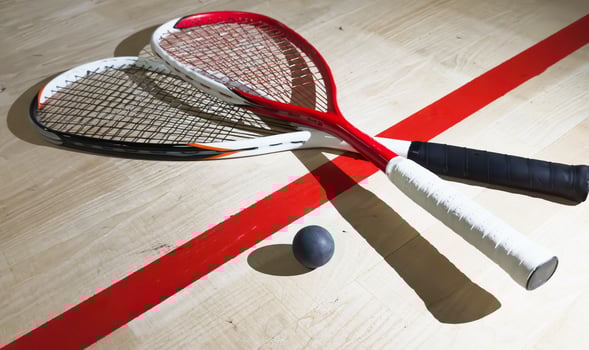 Two rackets and two squash balls lie on the parquet floor. Horizontal photo