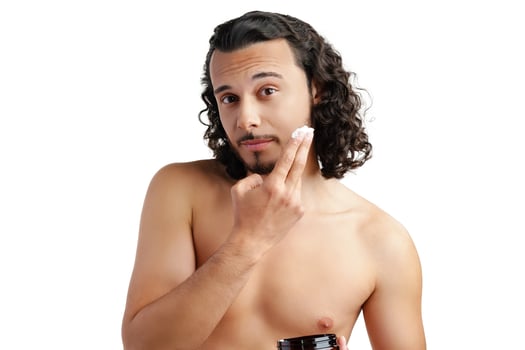A young man applying skincare cream on his face with a focused expression, demonstrating personal grooming at home photo