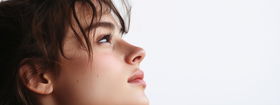Profile of a young woman gazing upwards with a serene expression against a plain background photo