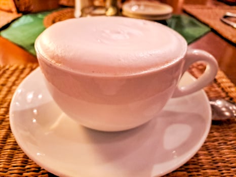 White offee cup and hot cappuccino on wooden table blurred background.Copy space photo