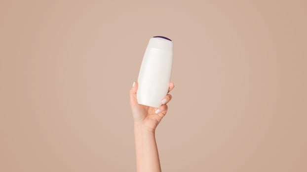 Girl showing bottle of shampoo, lotion or shower gel with mockup for design on pink background, closeup. Panorama photo