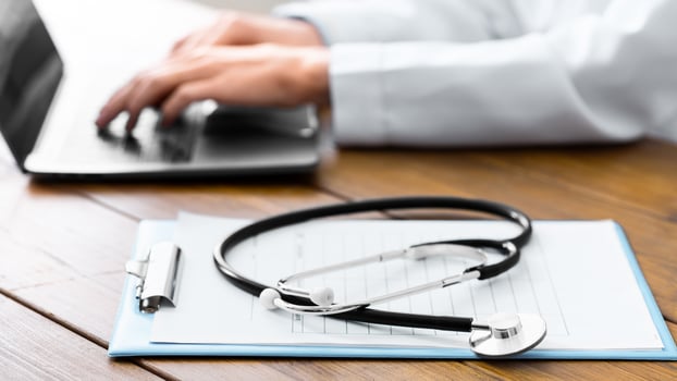 Online answers to patient questions. Stethoscope and tablet, hands of woman doctor typing on laptop on table, cropped photo