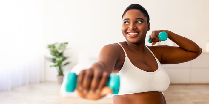 Home sports for weight loss. Happy plus size black woman doing fitness exercises with dumbbells indoors. Millennial overweight lady strengthening her biceps, leading active lifestyle photo