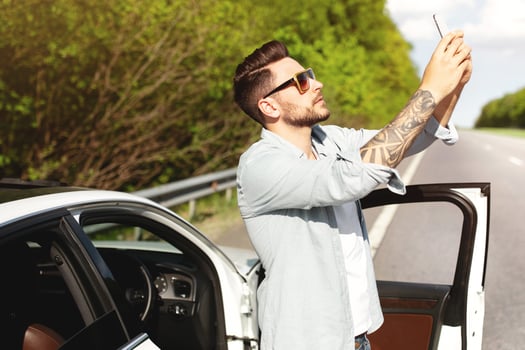 Unhappy Caucasian man standing near car, having problem with mobile connection, trying to find network on highway. Road emergencies, no signal, calling breakdown service concept photo