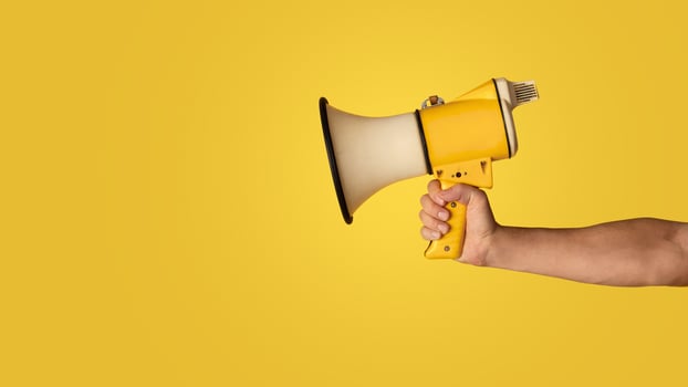 Advertising concept. Millennial guy holding loudspeaker on orange background, closeup. Panorama photo