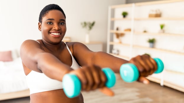 Domestic weightloss training. Positive curvy black woman doing exercises with dumbbells, strengthening her body at home. Plus size young lady working on her biceps muscles, staying healthy indoors photo