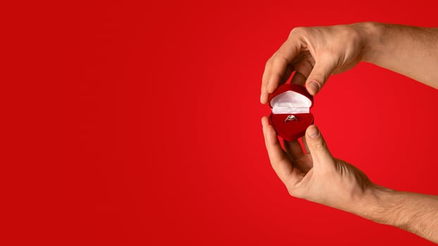 Male hands holding box with beautiful engagement ring on orange background, copy space. Panorama photo