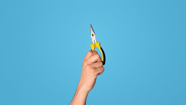 Cropped view of handyman holding flat nose pliers over blue background, closeup. Panorama photo