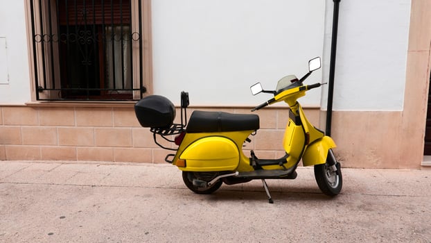 Yellow scooter parked by a wall on a quiet urban street photo