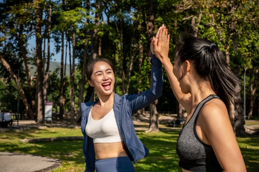 Two cheerful Asian friends give each other a high five while running together on a hot, sunny day. photo