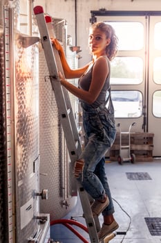 female winemaker controls the quality of wine on ladder over tank photo