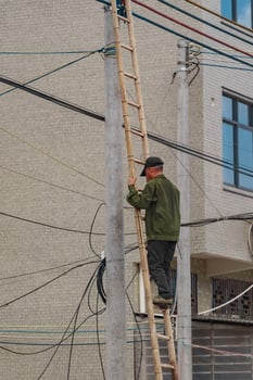 A worker is carefully climbing a sturdy ladder to make essential repairs on electrical wires photo