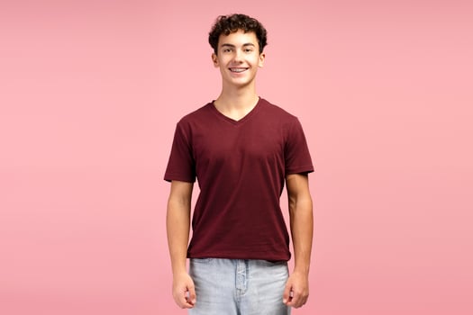 Smiling, attractive teen boy with braces wearing red t shirt, posing isolated on pink background photo